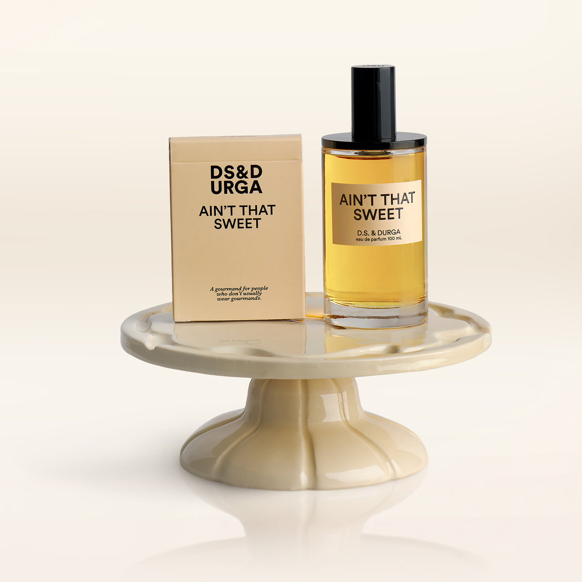 A 100 mL bottle of Ain't That Sweet perfume and flirt cards on a ceramic cake plate